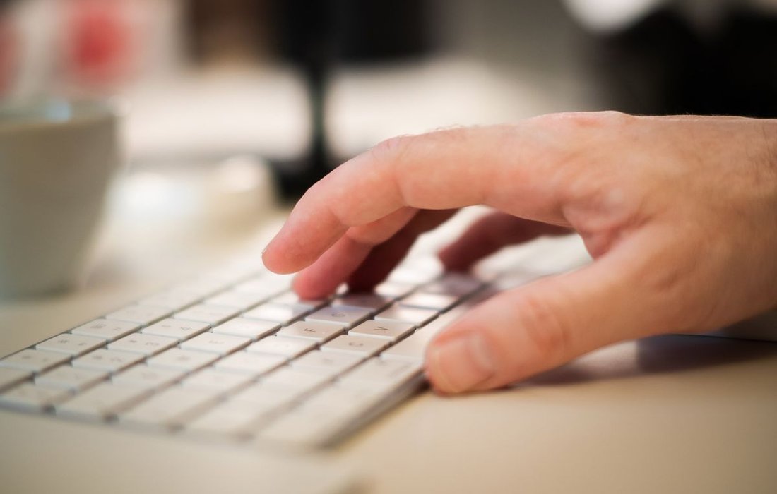 Hand typing on a keyboard at an office desk